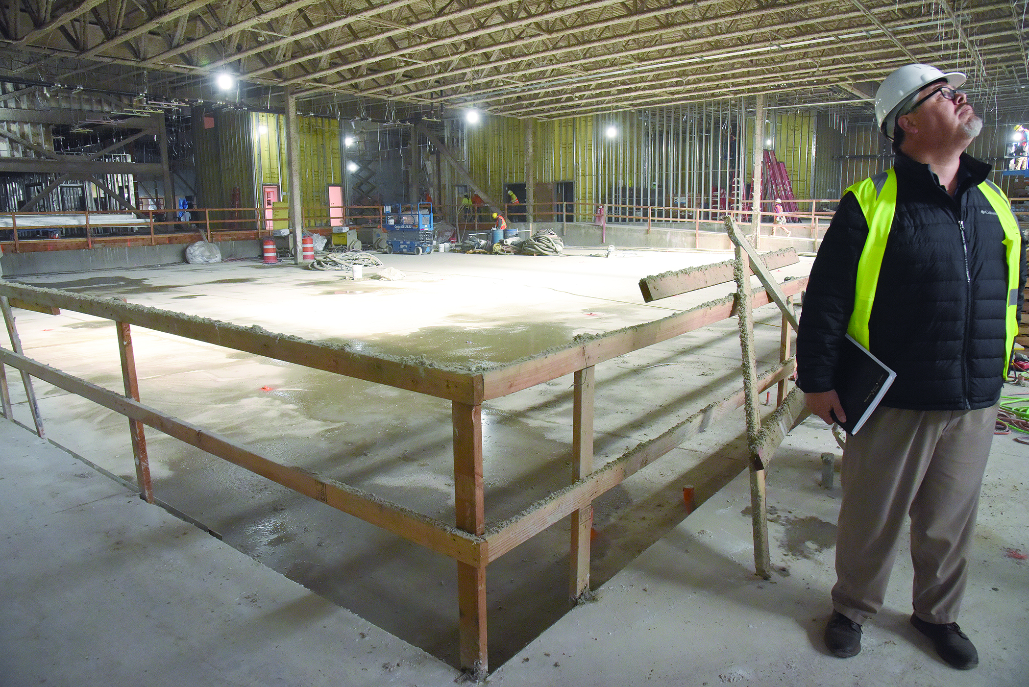 Inside a building under construction. A man, Dave Tovey, is on the far right of the frame wearing a hard hat and neon vest.