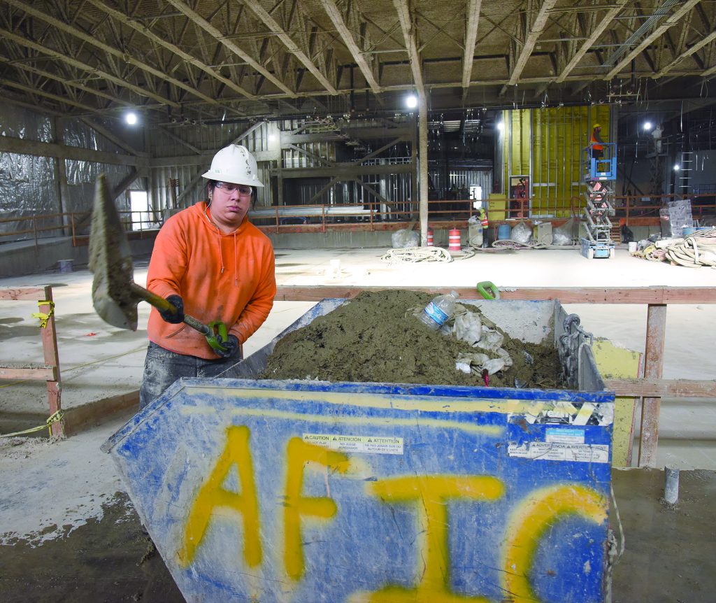 Marcus Looney shovels dirt off the concrete floor into a dump wagon inside the bowling alley construction site at Wildhorse Resort.