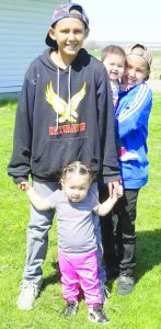 Boy stands in front yard with his siblings.