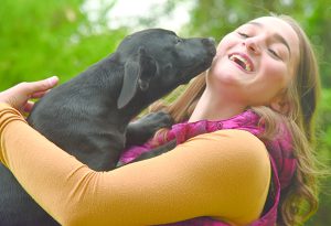 Teenager with her dog licking her face.